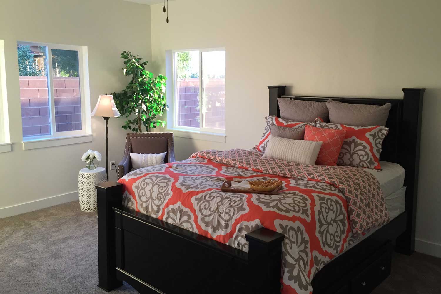 bedroom with beige carpet, queen bed and orange colored bedspread with sitting chair in the corner
