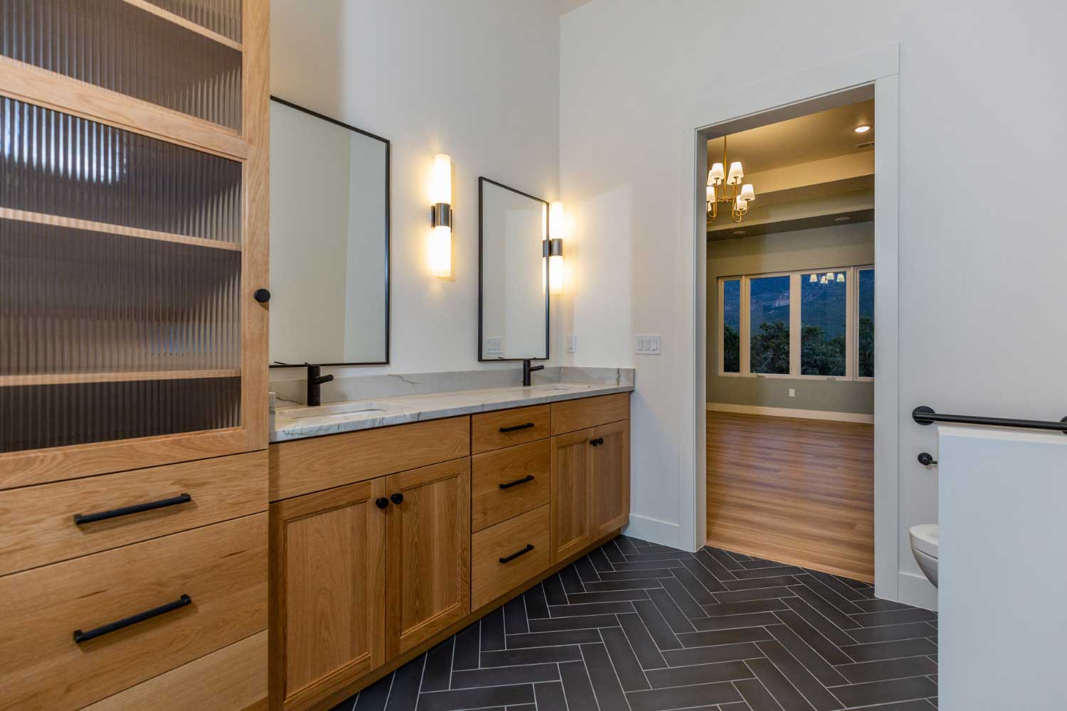 Primary bathroom with two sinks, glass cabinet, and vertical mirrors