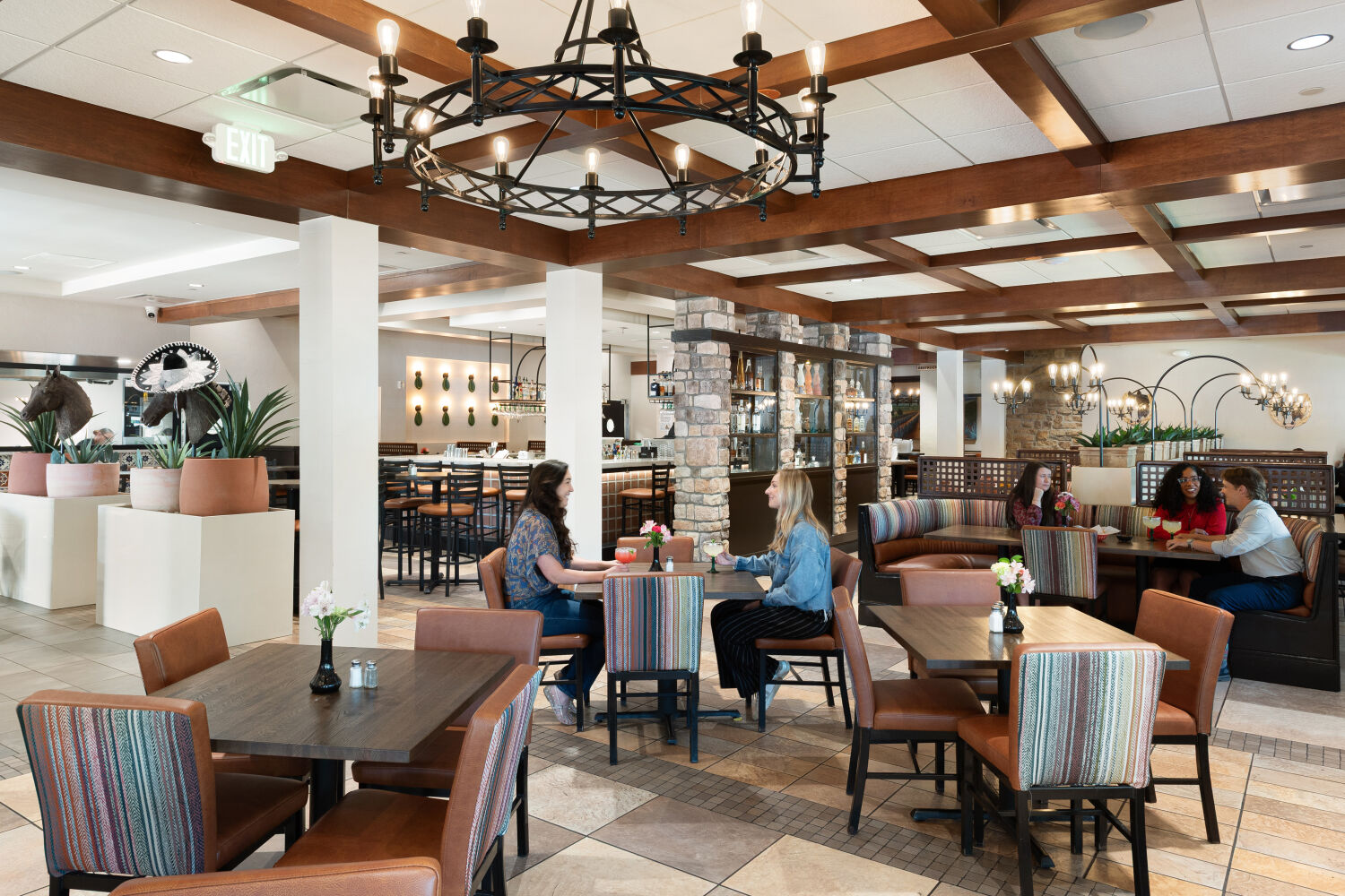 Spacious restaurant interior with wood‑beam ceilings, mixed booth and table seating, and diners gathered around tables.