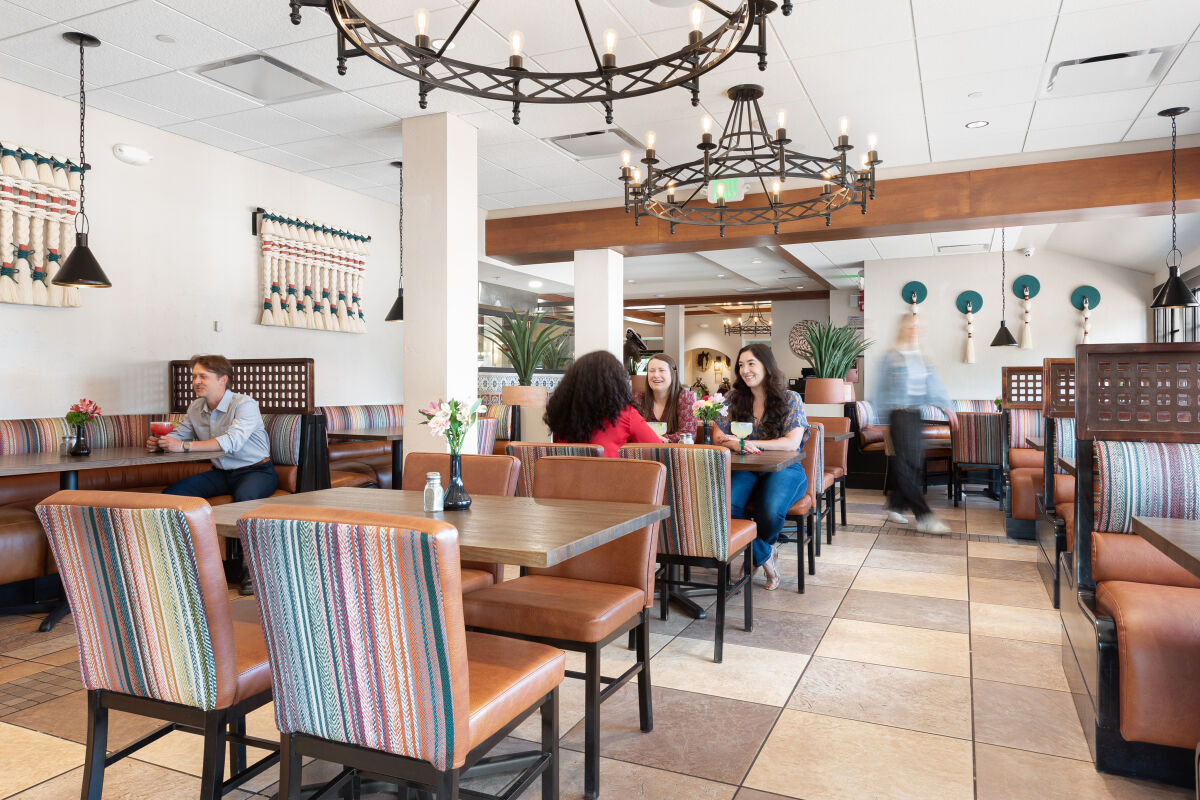 Dining area inside a Mexican restaurant with patterned booth seating, wooden tables, large wrought‑iron chandeliers, and groups of diners seated throughout the space.
