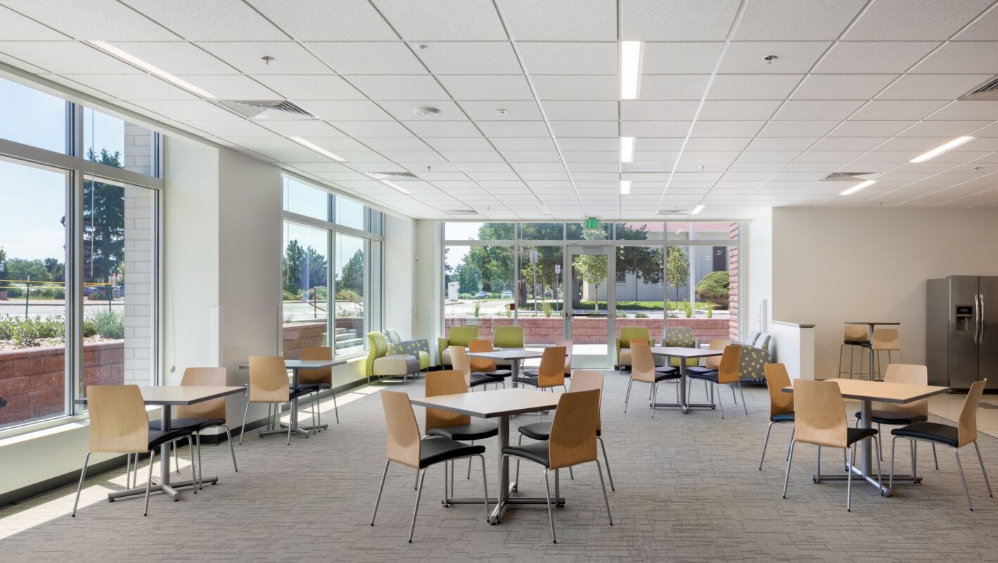 Common area at Bioscience 2 with round tables, wood chairs, lounge seating along the windows, and views of the landscaped exterior.