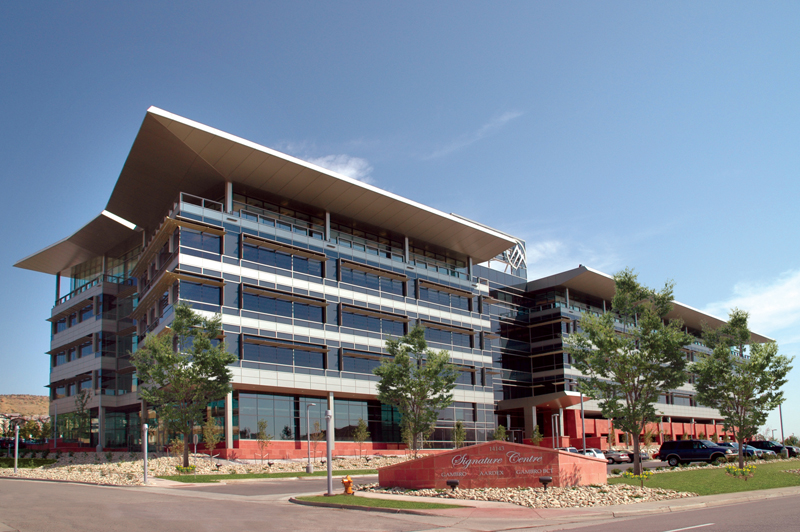 Daytime exterior view of a modern multi‑story office building with expansive glass façades, overhanging rooflines, and landscaped surroundings.