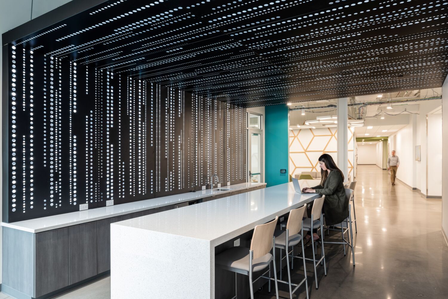 Collaboration bar inside of Bioscience 3 with a long counter, perforated black accent wall and ceiling, nearby glass meeting rooms, and an open corridor.