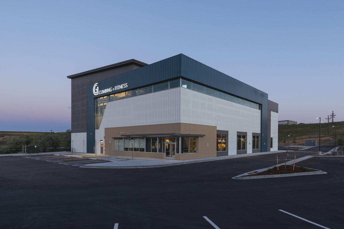 Exterior view of a modern climbing and fitness facility with metal panel siding and large windows at dusk.