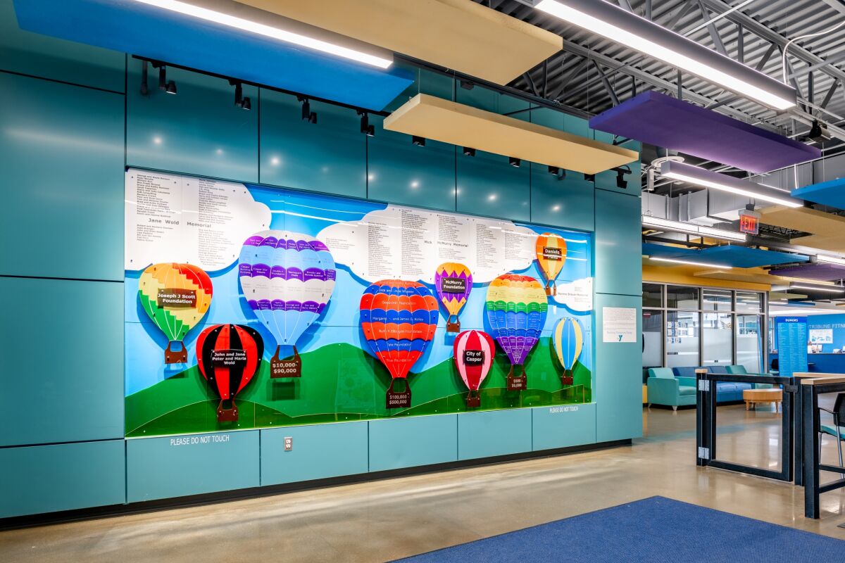 Lobby wall display featuring colorful hot‑air‑balloon artwork panels with donor names, set against teal accent walls and an open ceiling structure.