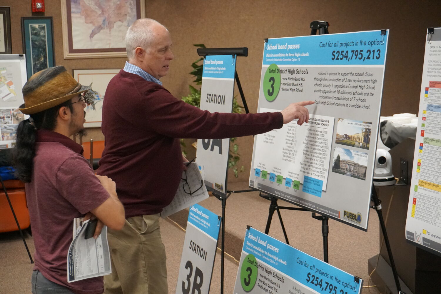 Public meeting display boards showing school bond options and cost information, with attendees reviewing the boards and informational posters arranged on easels.