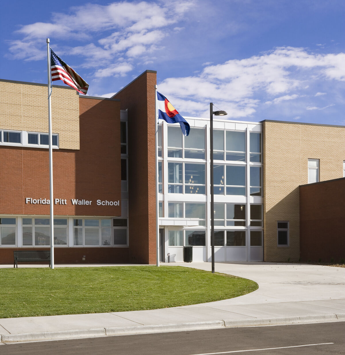 Exterior view of Florida Pitt Waller School with red brick and tan siding, tall glass entry façade, two flagpoles, landscaped lawn, and a curved walkway.