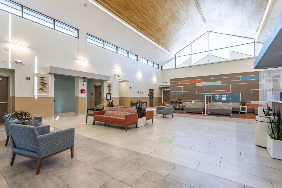 Lobby seating area with lounge chairs and sofas, a tall wood-paneled ceiling, tiled flooring, colorful acoustic wall panels, and clerestory windows.