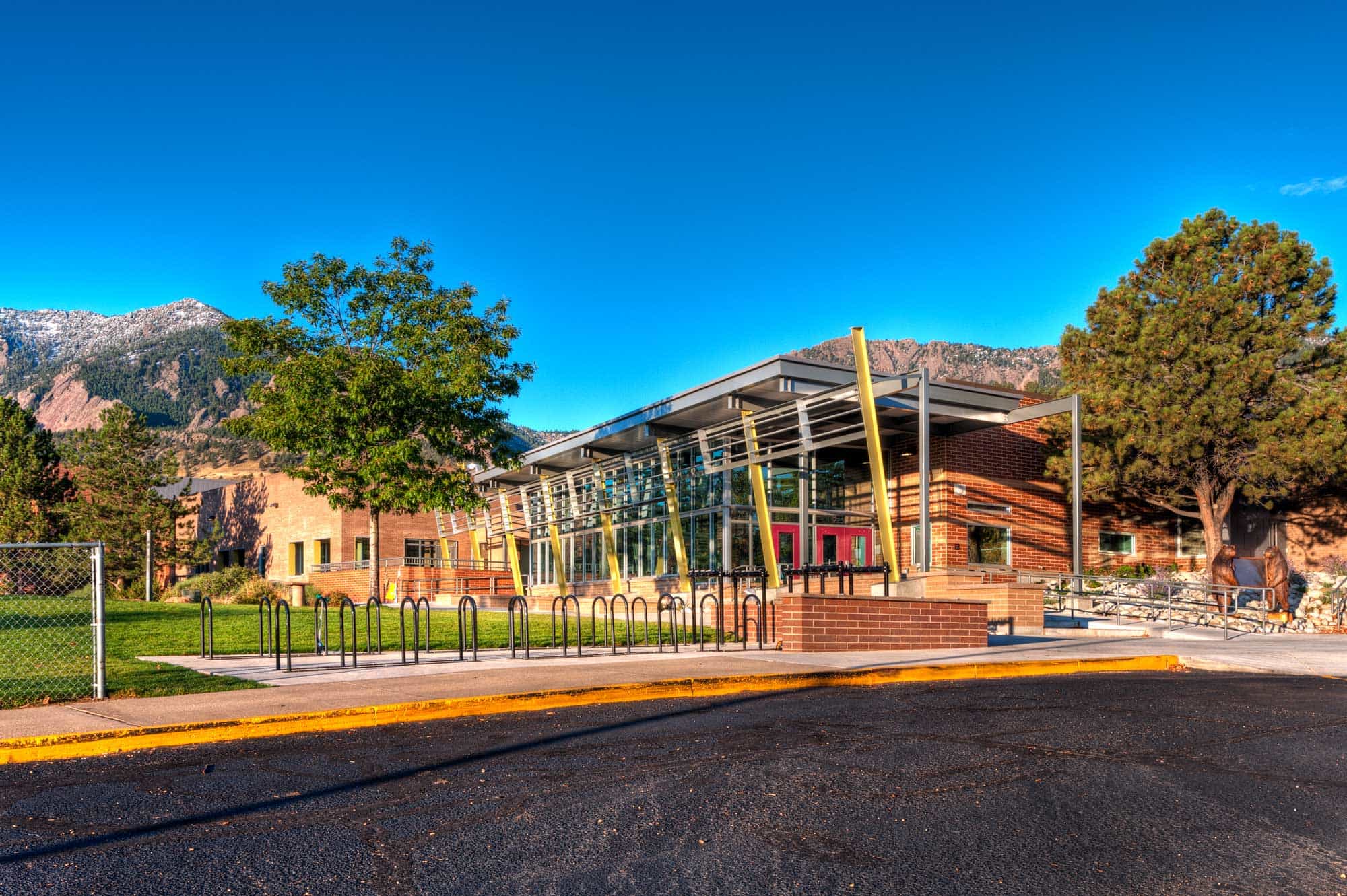 Exterior view of Bear Creek Elementary School, showcasing modern architectural design with large glass windows, clean lines, and a spacious outdoor area surrounded by lush greenery under a clear blue sky.