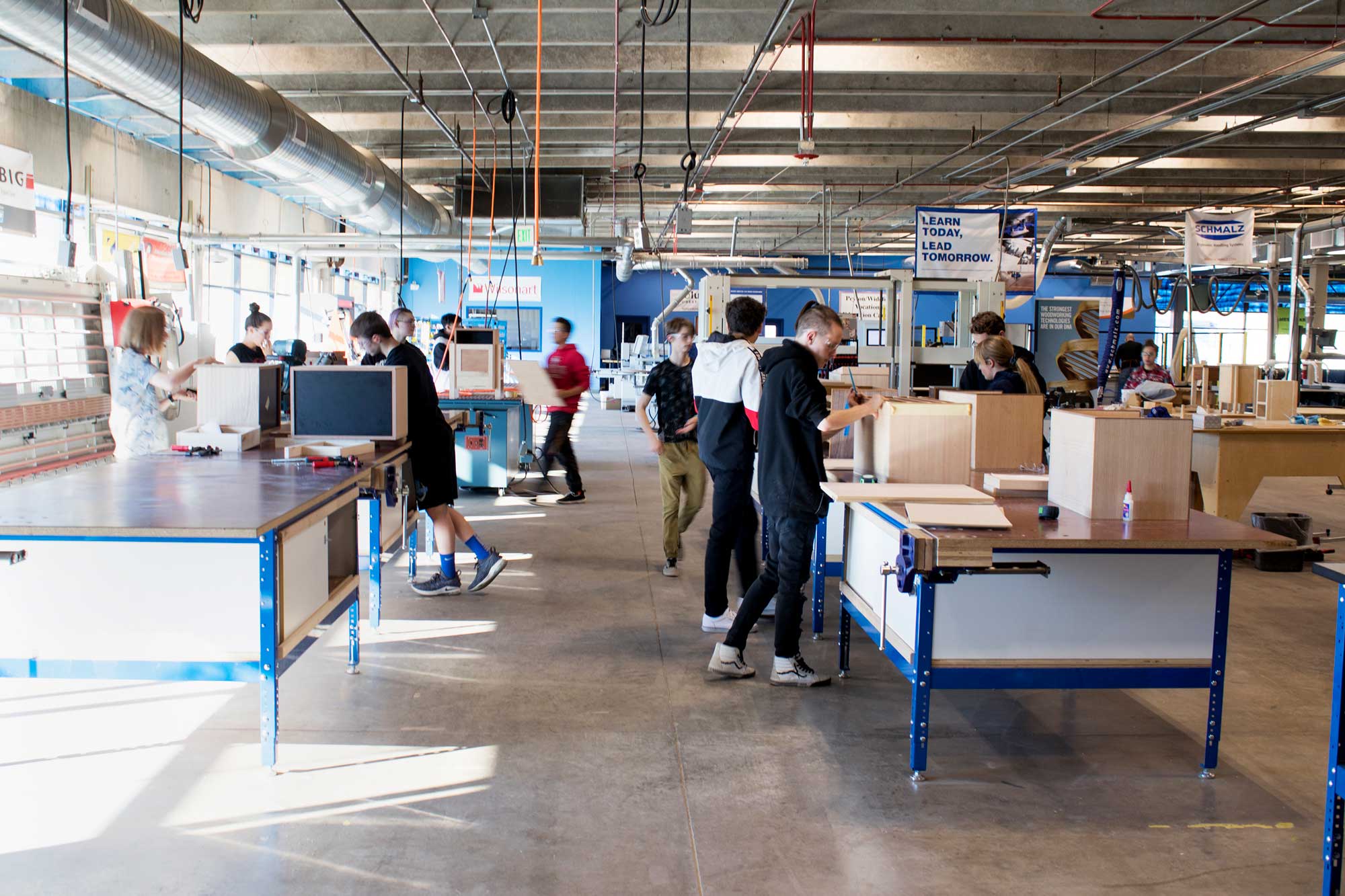 Interior view of a woodworking classroom at The MiLL, featuring spacious workstations, industrial equipment, and neatly arranged wooden materials. The well-lit space is designed for hands-on learning in manufacturing and craftsmanship.