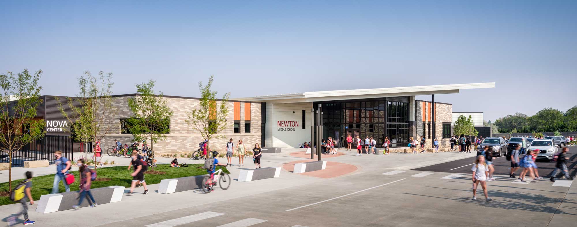 Exterior view of NMS showcasing a contemporary school building with a combination of brick and metal materials, large windows, and a welcoming entrance. The design emphasizes functionality and modern aesthetics in an educational setting.