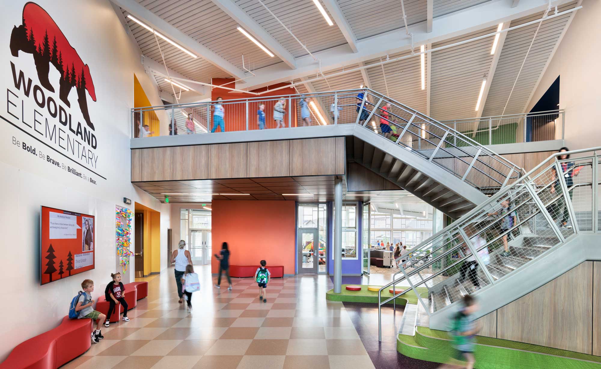 Interior view of Woodland Elementary School's entryway, featuring an open and welcoming design with high ceilings, large windows for natural light, and colorful accents. The space includes seating areas and modern finishes, creating a bright and inviting atmosphere for students and visitors.