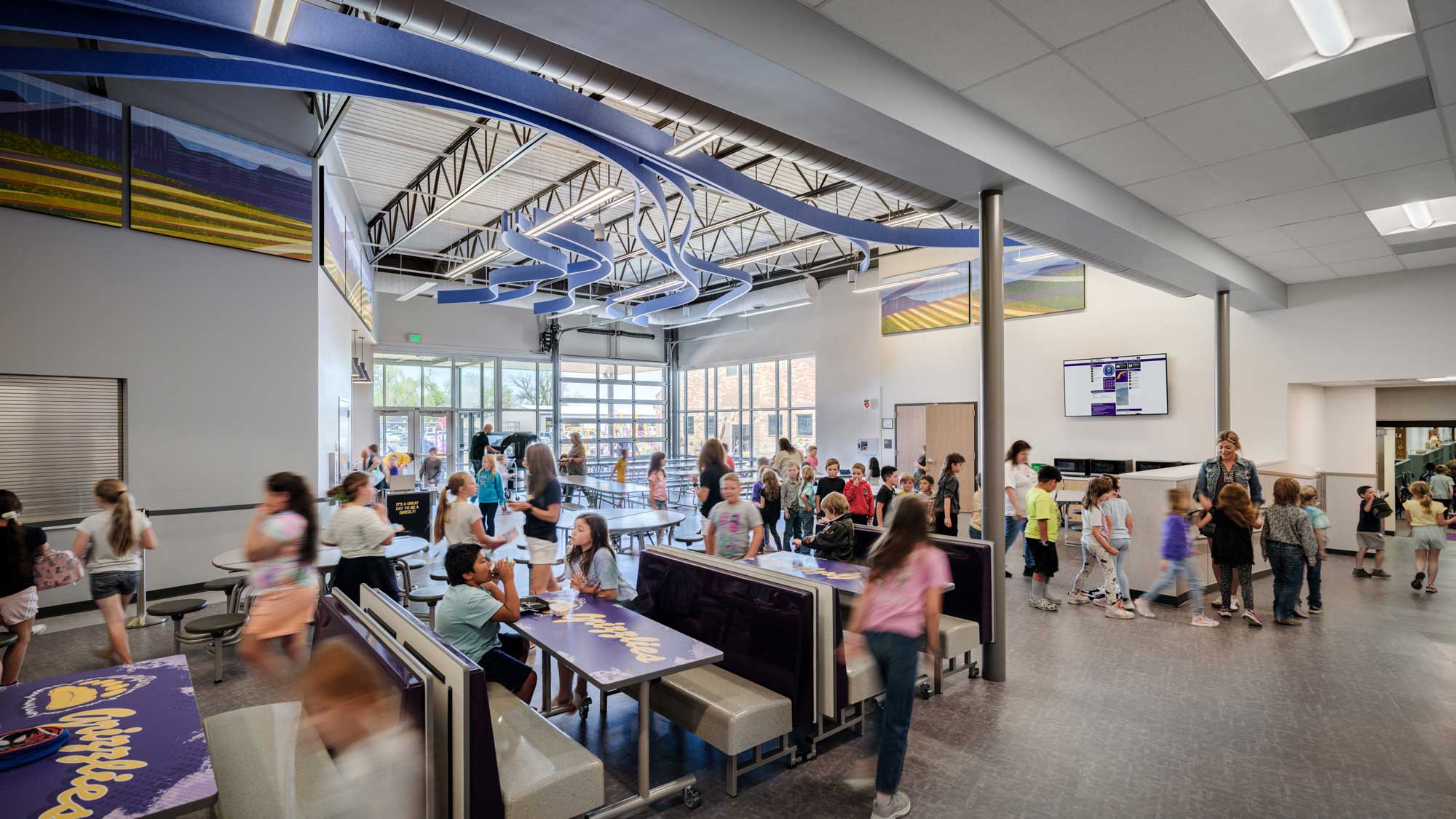 Interior view of Fowler High School commons area, featuring an open and spacious design with high ceilings, large windows for natural light, and a mix of seating options. The modern space fosters collaboration and community engagement for students.